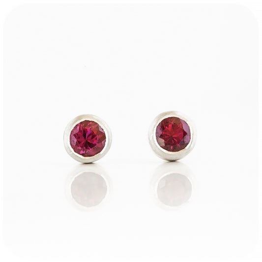 round cut pinkish red rhodolite stud earrings in a sterling silver bezel tube setting