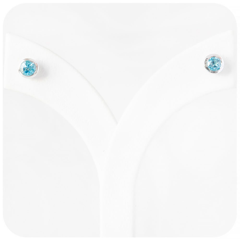 round cut swiss blue topaz stud earrings in a sterling silver bezel tube setting