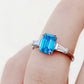Carmen, a Blue Emerald cut Trilogy Ring