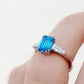 Carmen, a Blue Emerald cut Trilogy Ring
